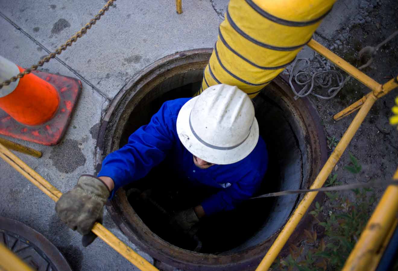 a picture of a man climbing out of a manhole with lots of safety equipment around the manhole